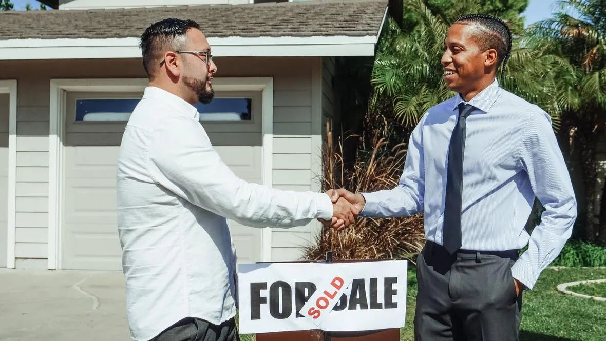 Realtor and client shaking hands in front of SOLD sign